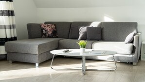 A modern living room with a grey sectional sofa, a round coffee table, and a small potted plant. - 'Villa Nordhang - Apartment 8' with Mountain View, Balcony & Wi-Fi (Winterberg)