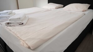 Ein ordentlich gemachtes Bett mit weißen Leinen und Kissen, ein schwarzer Kopfteil und eine Tür im Hintergrund.
