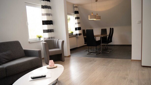 Ein modernes Wohnzimmer mit Sofa, Couchtisch, Essbereich mit Stühlen und einer Küche im Hintergrund.