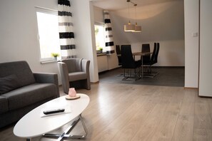 A modern living room with a sofa, a coffee table, a dining area with chairs, and a kitchen in the background. - 'Villa Nordhang - Apartment 9' with Mountain View & Wi-Fi (Winterberg)