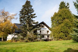 Un bâtiment à deux étages, dont l’inscription « Herdhang » est clairement visible sur la façade, entouré d’arbres et d’une zone herbeuse.