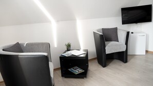 Ein modernes Wohnzimmer mit einer Couch, einem Sessel, einem Beistelltisch und einem an der Wand befestigten Flachbildfernseher.