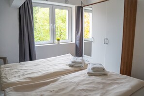Une chambre à coucher avec un lit, une fenêtre avec des rideaux, une petite plante sur le rebord de la fenêtre et un miroir sur le mur.
