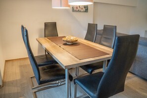 A dining table with a wooden top and black chairs, a bowl of food, and a wall-mounted lamp. - 'Villa Nordhang - Apartment 14' with Mountain View & Wi-Fi (Winterberg)