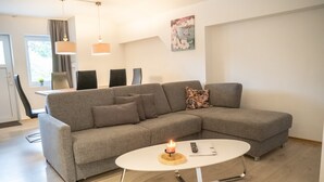 A modern living room with a grey sectional sofa, a white coffee table with a candle, and a painting on the wall.