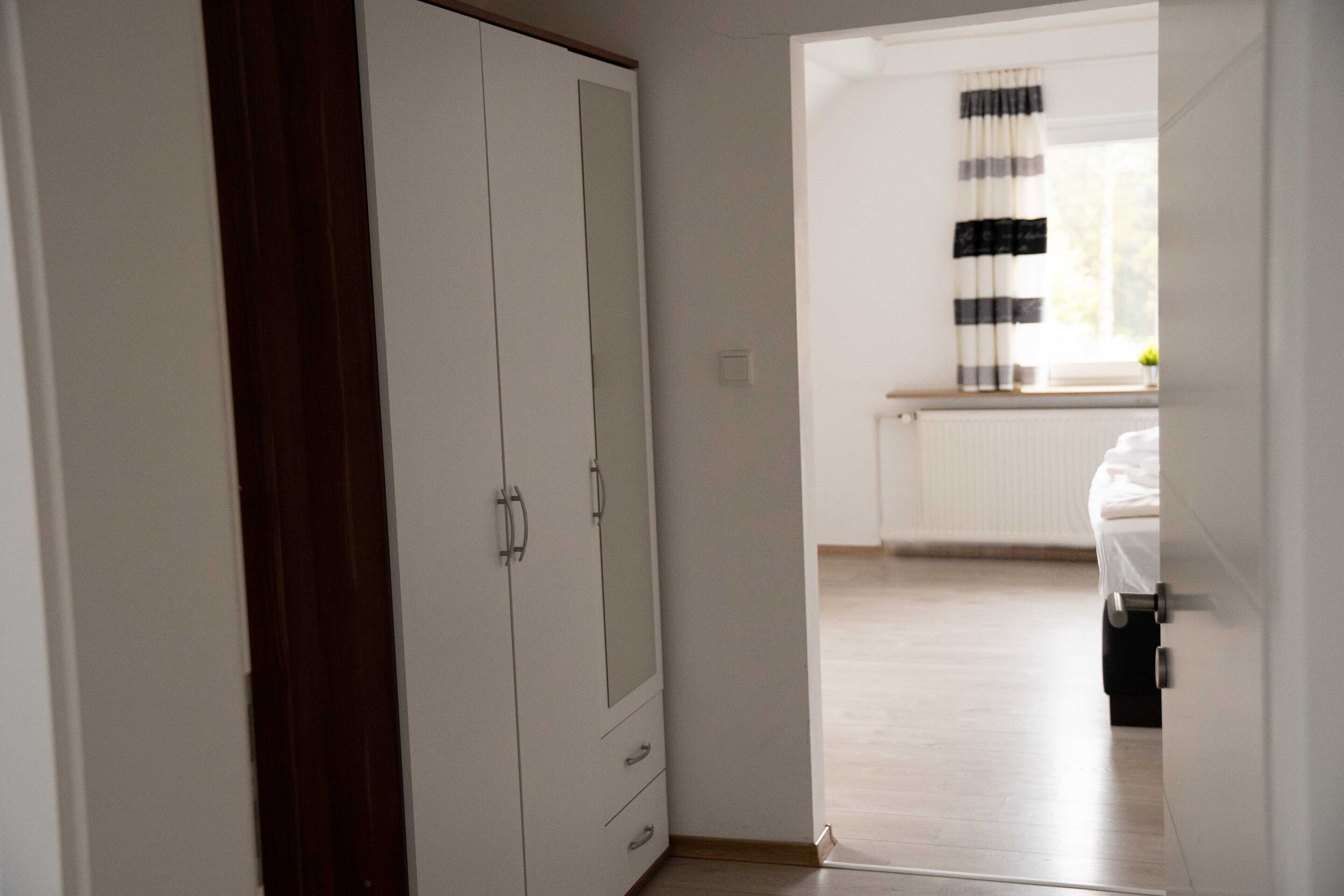 A bedroom with a bed, a window with curtains, and a wardrobe.