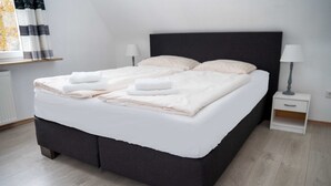 Una cama bien hecha con sábanas y toallas blancas, un cabecero oscuro y una mesita de noche con una lámpara.