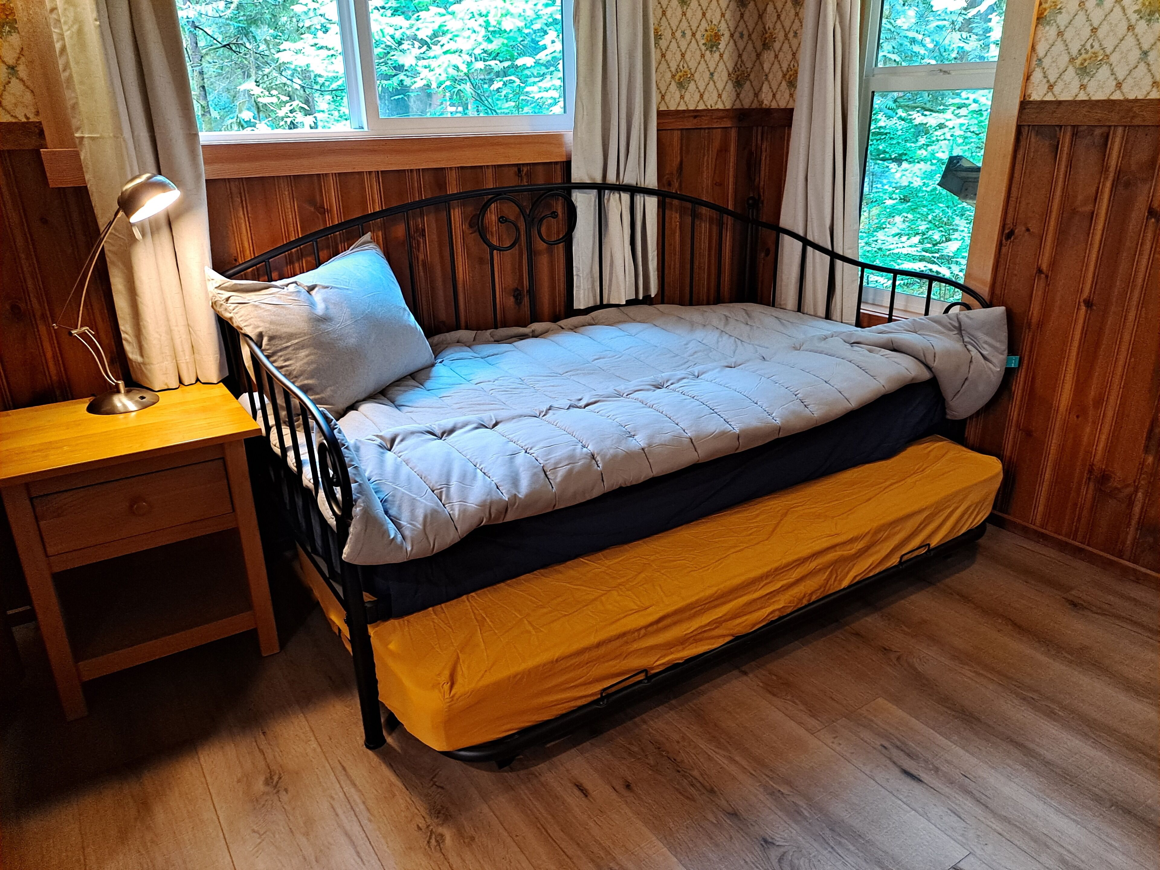 Una habitación de madera con una cama, una mesita de noche y una ventana.