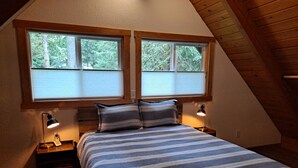 Ein Schlafzimmer mit einem Bett, zwei Nachttischlampen und zwei Fenstern mit Jalousien.
