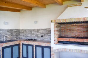 A kitchen with a built-in grill, stone backsplash, and dark cabinets.