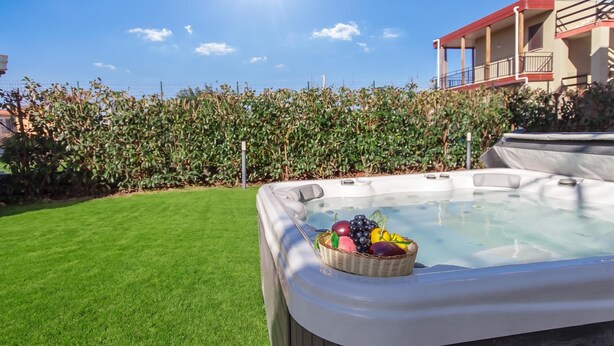 A hot tub with a basket of fruit on a well-maintained lawn, surrounded by a fence and a building with balconies. - Eclisse House Few Steps From The Sea, Augusta, Italy (Augusta)