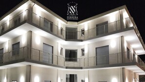 Un hôtel à plusieurs étages, doté de balcons, d’un escalier central et d’un logo au sommet.