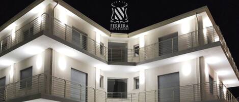 A multi-story hotel with balconies, a central staircase, and a logo at the top.
