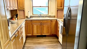 A modern kitchen with wooden cabinets, a stainless steel refrigerator, a window with a view, and a black rug. - Beach House ∆ Prime Location ∆ Steps to the Ocean (Old Orchard Beach)