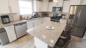 Una cocina moderna con armarios blancos, encimeras de granito, electrodomésticos de acero inoxidable y una isla central con asientos.