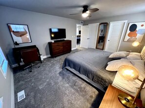 Una camera da letto con un letto, una cassettiera, una TV e una ventola a soffitto.