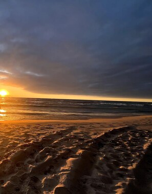 Una spiaggia con impronte che conducono all'acqua, un tramonto sullo sfondo e un cielo nuvoloso.
