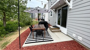 Un patio con mesa y sillas de madera, una sombrilla y guirnaldas de luces.