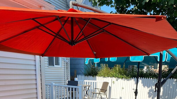Een terras met tuinmeubilair, waaronder een bank en een tafel, en een rode parasol.