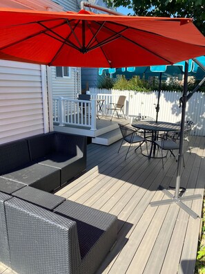A deck with outdoor furniture, including a sofa and a table, and a red umbrella. - Cheerful 5 bed Residential house. (Bridgeport)