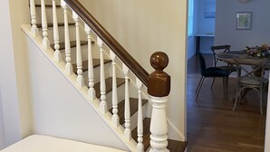 Een trap met witte balustrades en een houten leuning, die leidt naar een kamer met een houten vloer en een eethoek in de achtergrond.