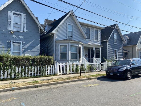 A row of two-story houses with white picket fences, a street, and a parked car. - Cheerful 5 bed Residential house. (Bridgeport)