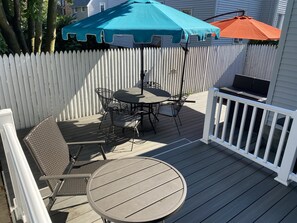 A deck with a table and chairs, a blue and orange umbrella, and a white picket fence. - Cheerful 5 bed Residential house. (Bridgeport)