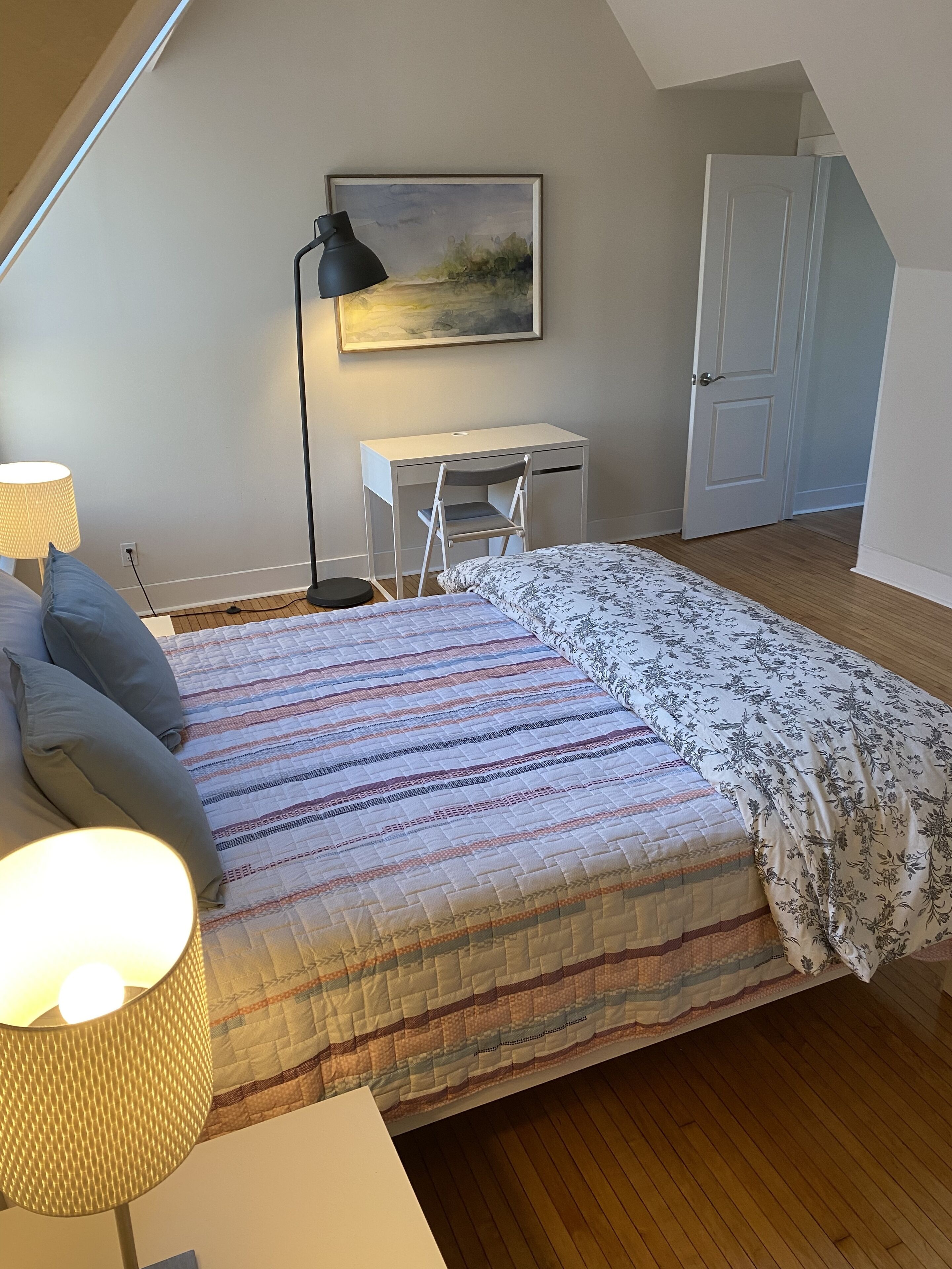 Un dormitorio con una cama, un escritorio, una silla, una lámpara y una puerta.