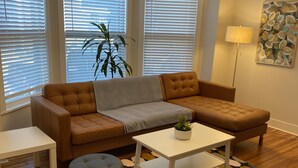 Een moderne woonkamer met een bruine bank, een witte salontafel, een zwart voetenbankje en een kamerkleed met een patroon.