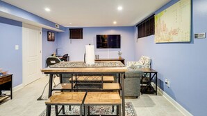 Ein Essbereich mit Holztisch und Bänken, einem an der Wand montierten Fernseher und einem Stadtbild-Kunstwerk.