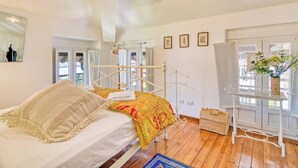 A bedroom with a bed, a window, a white metal bed frame, a white wall, and a small table with a vase. - Piccolo Mondo Antico: Stresa 2BR Apartment with Lake View, Stresa, Italy (Stresa)