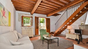 A living room with a sofa, a green armchair, a coffee table, a cabinet, a lamp, and a staircase.