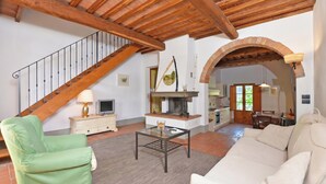 A spacious living area with a wooden staircase, a fireplace, a dining area, and a kitchen visible through an archway. - Francigena 4, Castelfiorentino, Italy (Castelfiorentino)