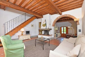 Amplia sala de estar con una escalera de madera, una chimenea, un comedor y una cocina visible a través de un arco.