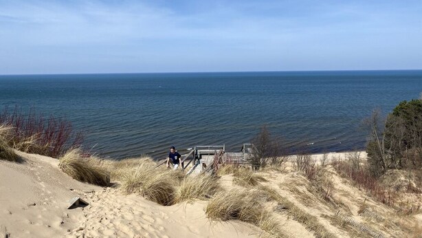 A beach with a wooden walkway leading to the water, surrounded by sand dunes and sparse vegetation.