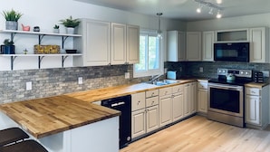 A modern kitchen with white cabinets, a wooden countertop, and a brick backsplash.