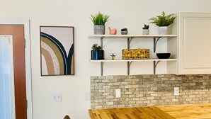 A modern kitchen with a wooden table, two chairs, a brick backsplash, and shelves with plants and kitchenware.