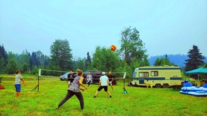A group of people playing volleyball in a grassy field with a camper and RVs in the background. - Spacious Lakefront Campsites (Lone Butte)