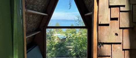 A triangular attic bedroom with a large window overlooking a garden and a body of water.