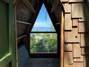 Ein schrägwangiges Schlafzimmer im Dachgeschoss mit einem großen Fenster mit Blick auf einen Garten und ein Gewässer.