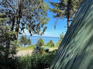 A view of a coastal area with a clear sky, a body of water, and a grassy area with trees. - A-Frame Shelter (T15)  - Oceanside Views (Port Angeles)