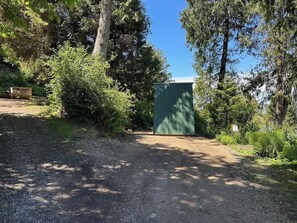 A gravel path leading to a green building surrounded by dense trees. - A-Frame Shelter (T15)  - Oceanside Views (Port Angeles)