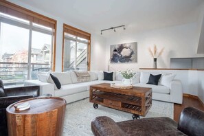 Uma sala de estar moderna com um sofá seccional, uma mesa de centro de madeira e uma janela grande.