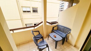 A balcony with two chairs and a small table, a window with a view of buildings, and a railing. - Sunbay City Rooms (Larnaca)