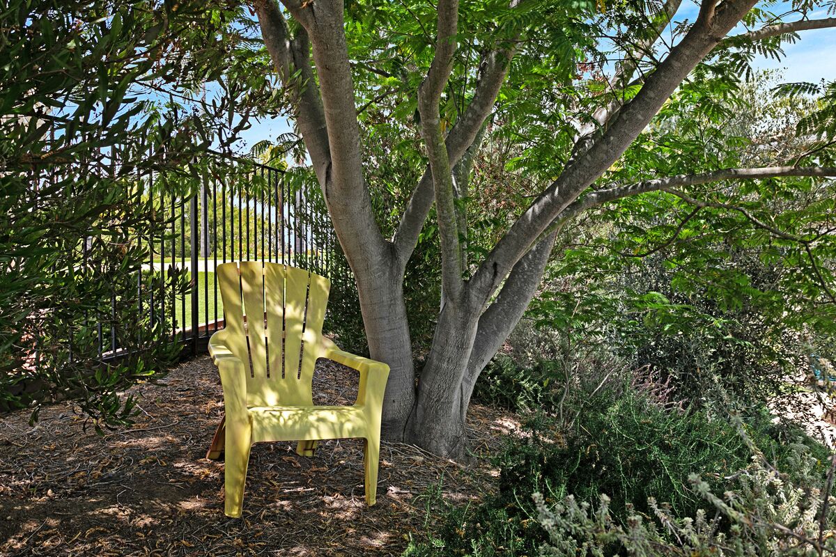 A yellow plastic chair under a tree in a garden area.