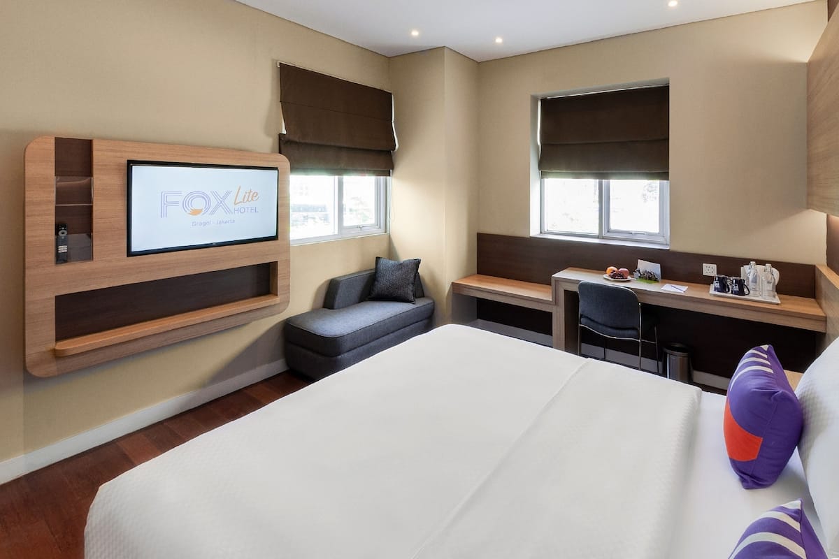 Une chambre d’hôtel comprenant un lit, un bureau, une chaise, un téléviseur fixé au mur et une fenêtre.