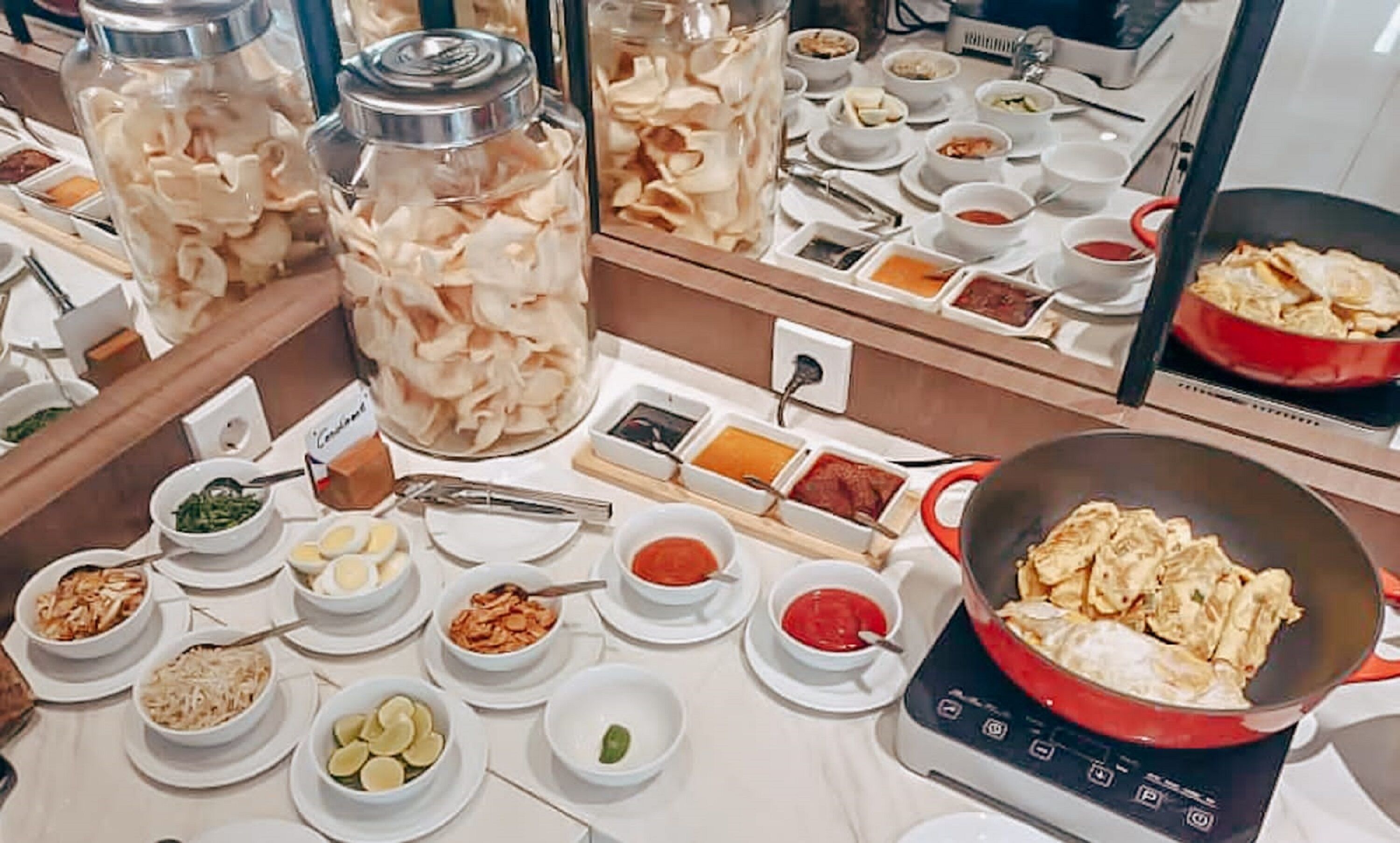 Disposição de buffet com diversos pratos, incluindo um wok com comida, potes de alimentos em conserva e pequenas tigelas de acompanhamentos.