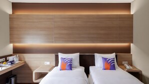 A hotel room with two beds, a desk with a chair, a nightstand with a phone, and a wall-mounted panel. - FOX Lite Hotel Grogol Jakarta (Jakarta)