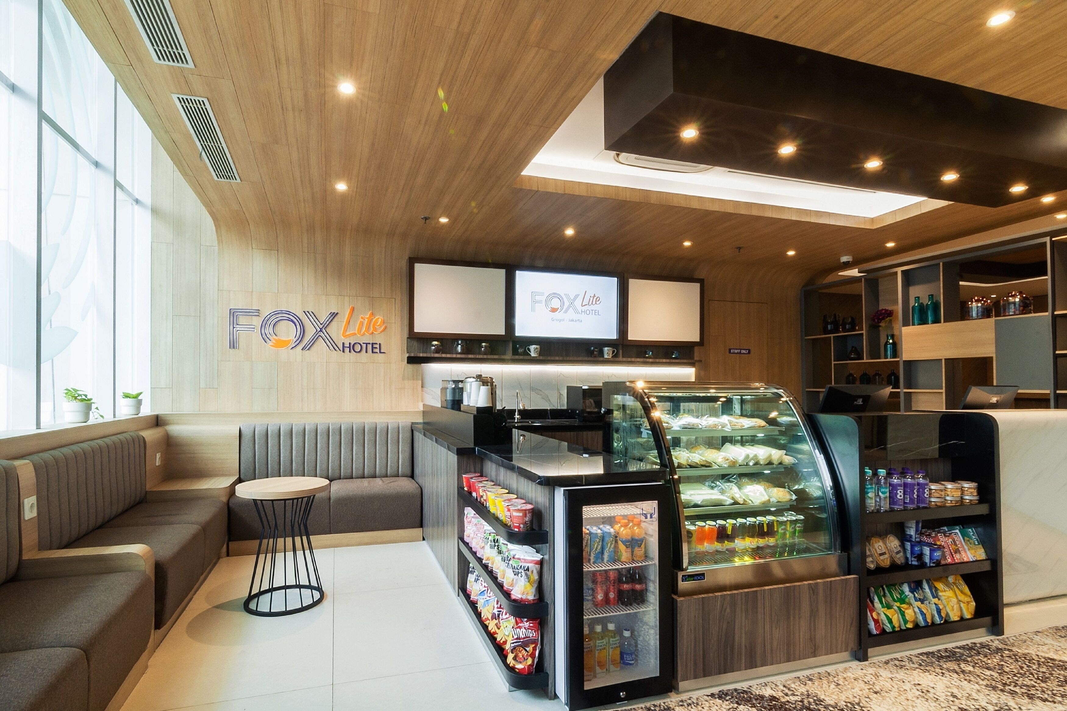 Un moderno vestíbulo de hotel con zonas de estar, una estación de bebidas y una pantalla digital.