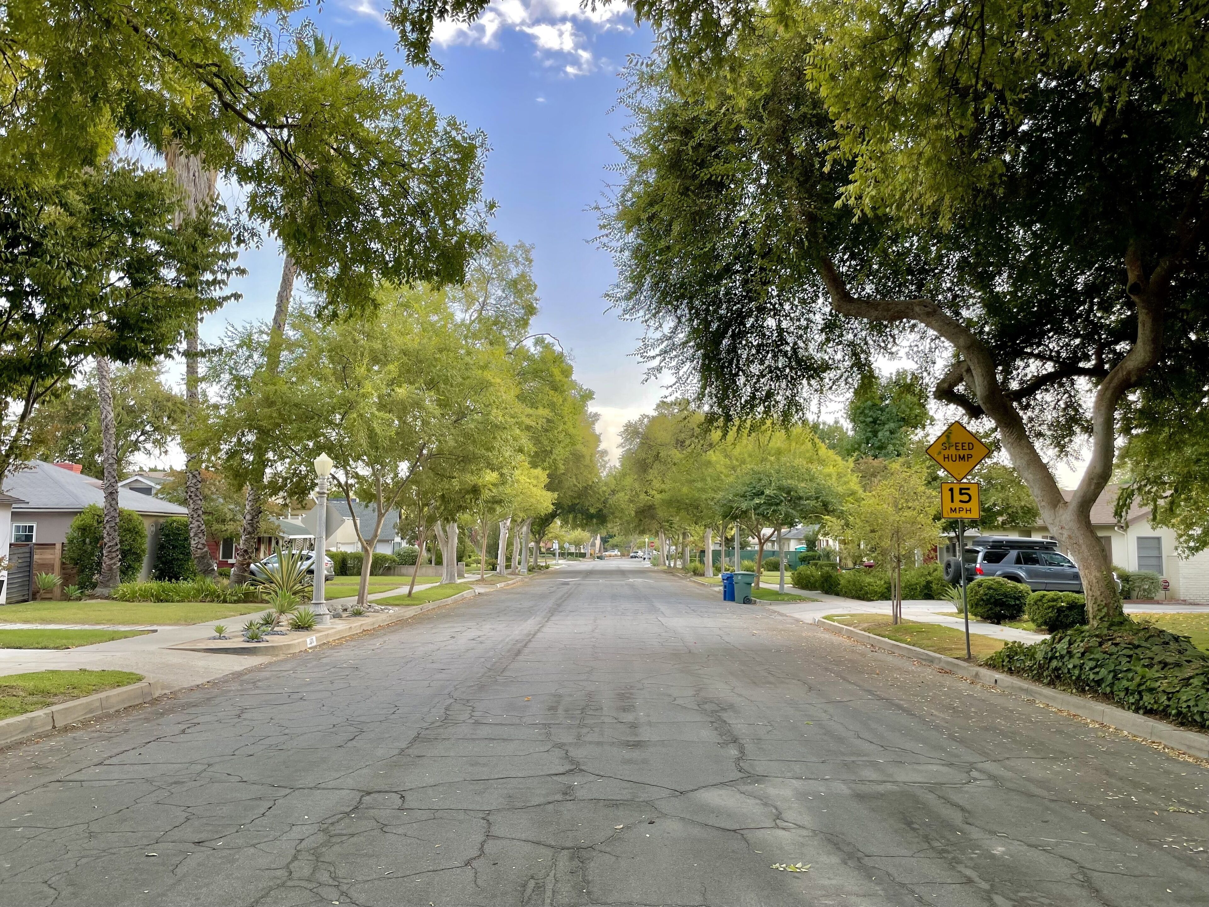 Une rue résidentielle bordée d’arbres et de maisons, avec un panneau indiquant une zone limitée à 15 miles par heure (environ 24 km/h).